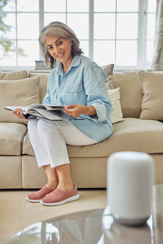 A woman Sitting On a Sofa speaking to a digital assistant.