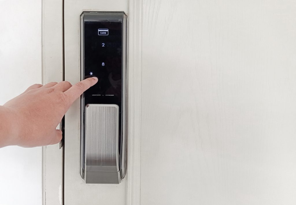 A hand entering password code on a smart digital touch screen keypad to lock and unlock a door.